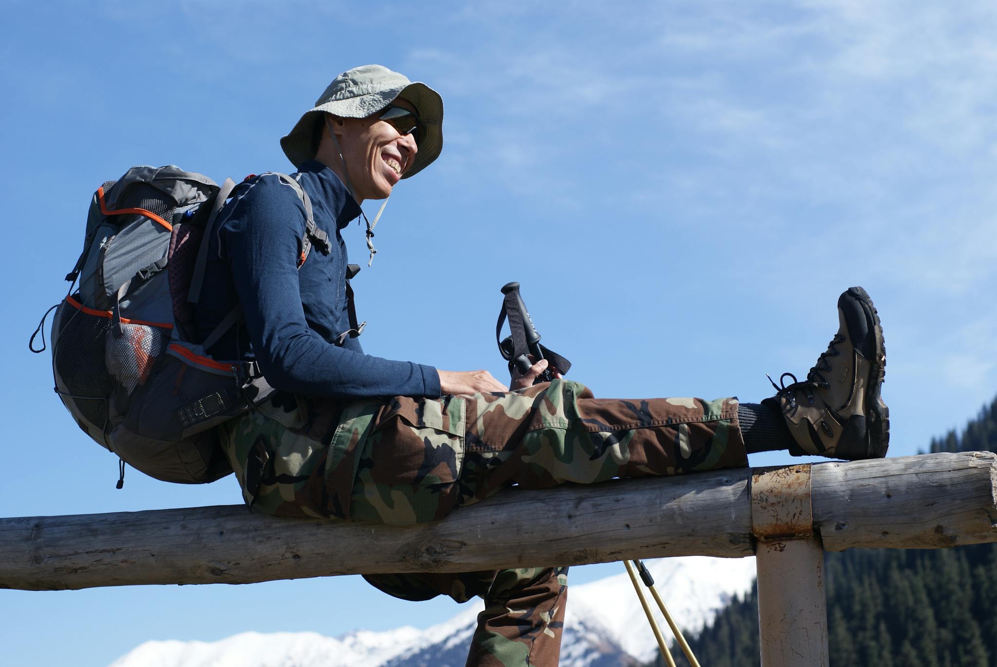 Smiling hiker with backpack resting on a fence with a stunning mountain view.