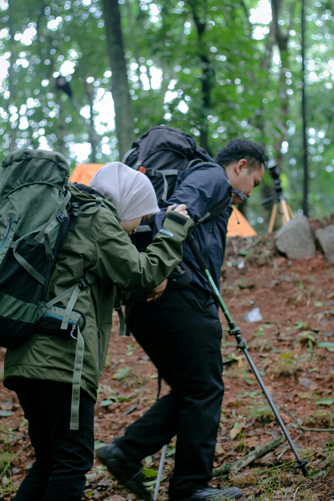 Two hikers with backpacks trekking in a forest with camping gear.